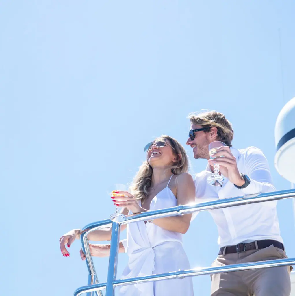 A couple in white clothes drinking champagne on a boat.