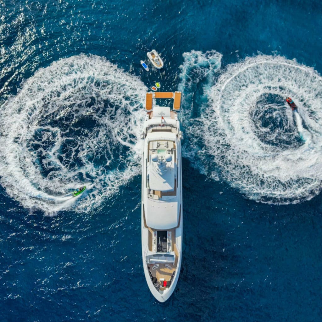 A yacht with three jet skis creating circular wakes in the ocean.