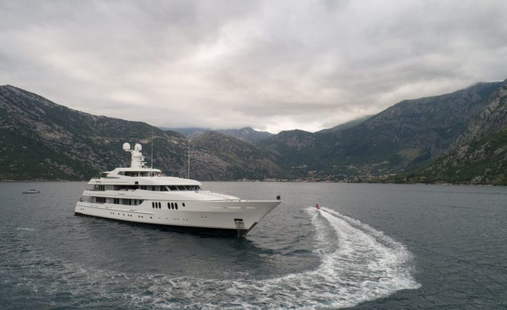 A large white yacht on a sea with mountains in the background.