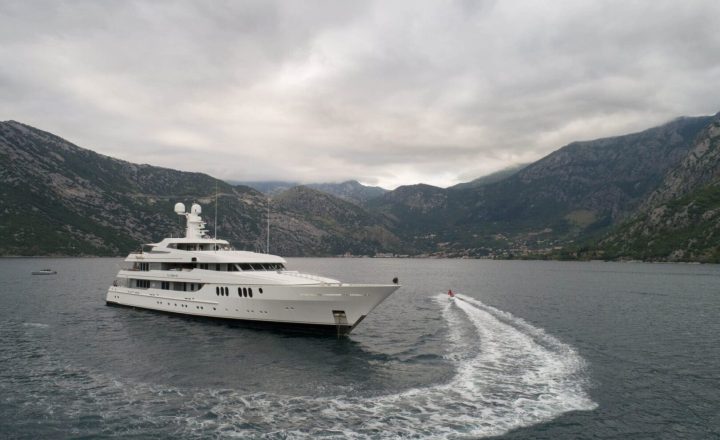 A large white yacht on a lake surrounded by mountains.